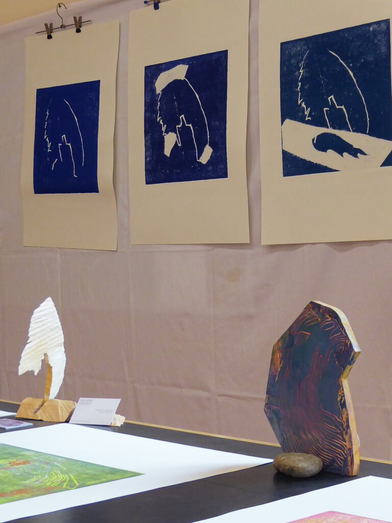 Ausstellungsansicht, drei blaue Holzschnitte  vom selben Grundmotiv im Weißlinienschnitt mit der Anmutung, dass ein Flügel provisorisch gebaut wird. 
Arbeitstitel ist Ikarus und der Traum vom Fliegen. 